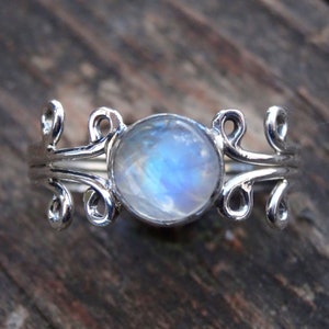 May include: A silver ring with a delicate, swirling design and a round, iridescent moonstone.