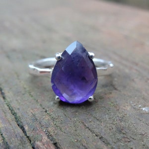 May include: A silver ring featuring a large, faceted, pear-shaped amethyst gemstone.