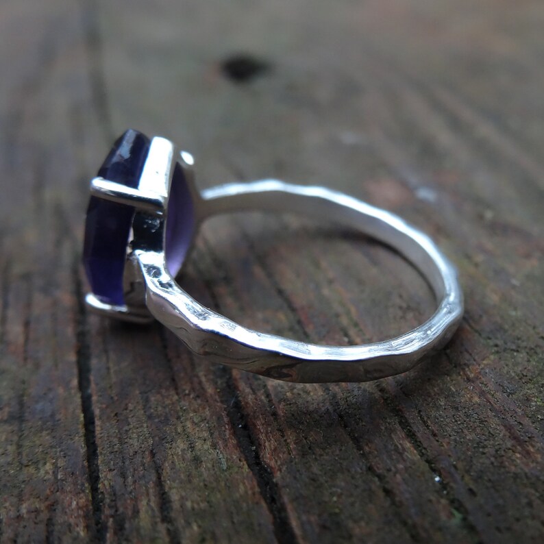 May include: A silver ring featuring a large, faceted, purple gemstone. The ring band is textured and has a hammered finish.
