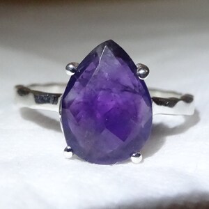 May include: A silver ring featuring a large, faceted amethyst gemstone in a pear shape.