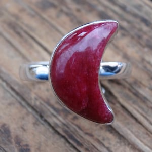 Peut inclure: Une bague en argent avec une pierre précieuse rouge en forme de croissant de lune.
