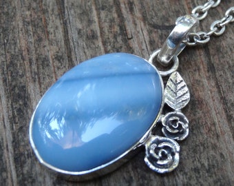 May include: A silver pendant necklace with a light blue oval opal stone and a silver floral design with leaves and roses.