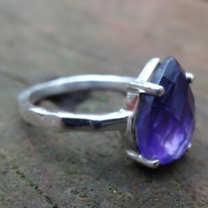 May include: A silver ring featuring a large, faceted amethyst gemstone. The ring has a hammered band and a simple setting.