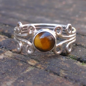May include: A silver ring with a brown and gold tiger's eye gemstone set in a delicate, swirling design.