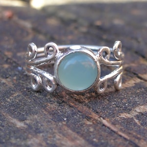 May include: A silver ring with a delicate, swirling design and a light blue gemstone in the center.
