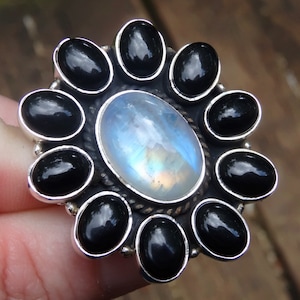 May include: A silver ring with a large oval moonstone surrounded by a circle of smaller black stones.