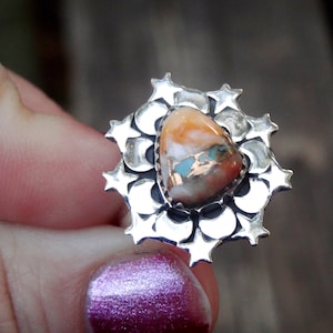 Puede incluir: Un anillo de plata con una piedra grande multicolor engastada en un diseño de estrella.