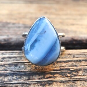 May include: A silver ring featuring a large, pear-shaped gemstone. The stone has a light blue color with swirling white and darker blue patterns. The ring's band is a simple, thin silver band.