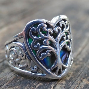 May include: A silver ring with a heart-shaped design featuring a tree of life with green and blue abalone inlay.