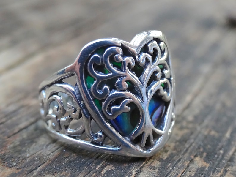 May include: A silver ring with a heart-shaped design featuring a tree of life with green and blue abalone inlay.