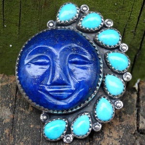 May include: A silver pendant with a carved lapis lazuli moon face surrounded by turquoise stones.