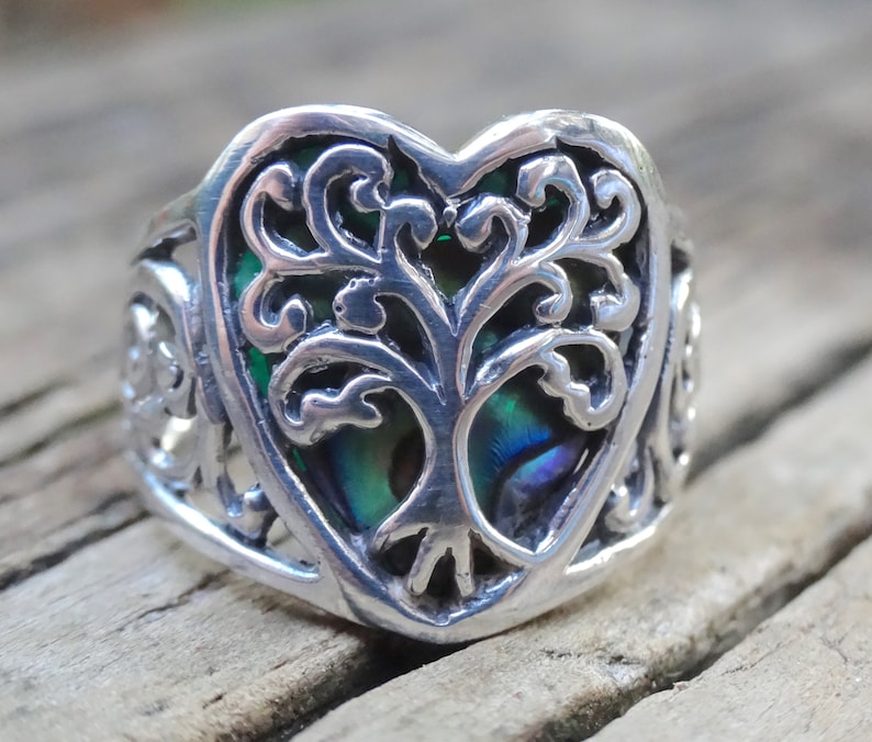 May include: A silver ring with a heart-shaped design featuring a tree of life with a green and blue abalone shell inlay.