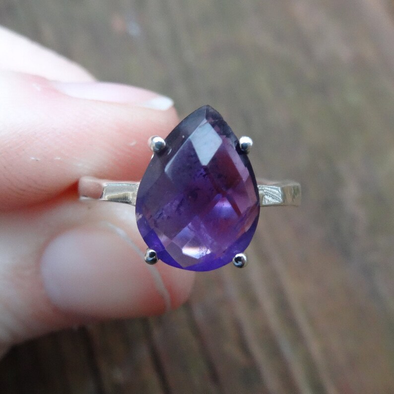 May include: A silver ring featuring a large, faceted amethyst gemstone in a pear shape.