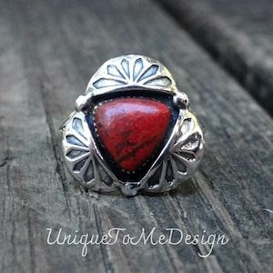 May include: A silver ring with a triangular red stone. The ring has a decorative design around the stone and the text "Unique To Me Design" is visible in the image.