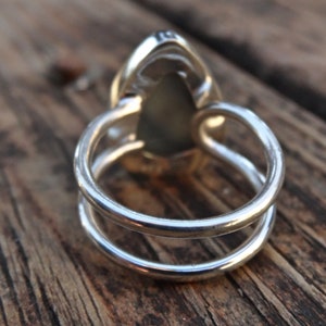 May include: A silver ring with a pear-shaped, light green gemstone. The ring has a double-band design, with two parallel bands forming the ring's base. The gemstone is set in a silver bezel.