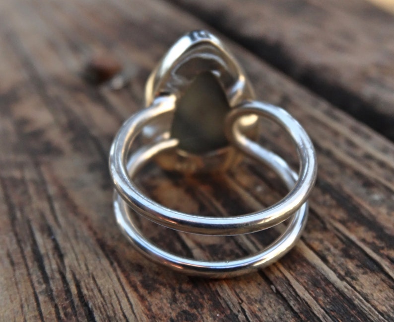 May include: A silver ring with a pear-shaped, light green gemstone. The ring has a double-band design, with two parallel bands forming the ring's base. The gemstone is set in a silver bezel.