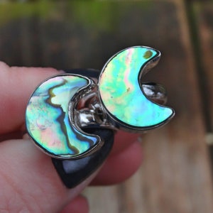 May include: A silver ring featuring two iridescent abalone shell crescent moons. The moons are set in silver and have a blue, green, and pink iridescent sheen.
