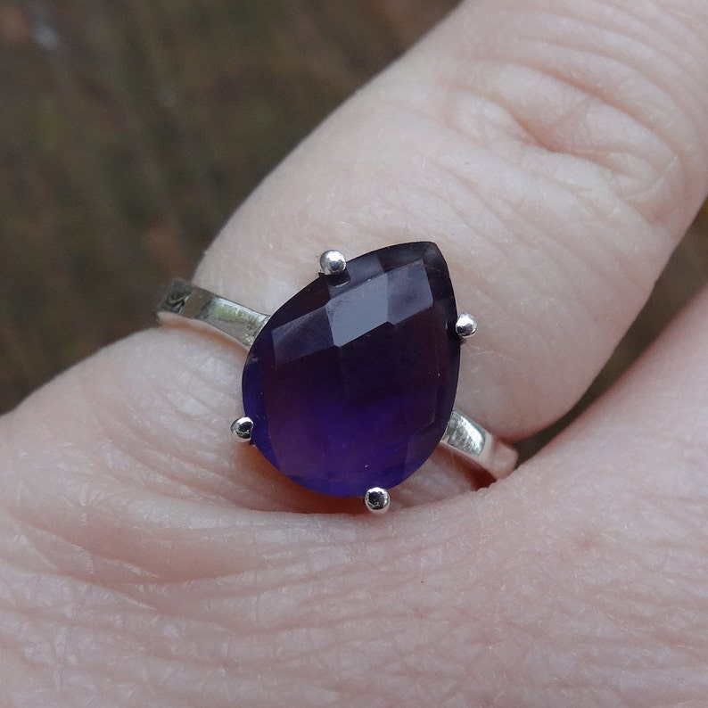 May include: A silver ring with a teardrop-shaped purple gemstone.
