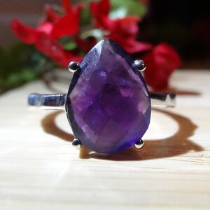 May include: A silver ring featuring a large, pear-shaped amethyst gemstone. The gemstone is a deep purple colour and has a faceted cut.