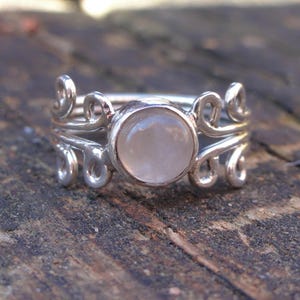 May include: A silver ring with a delicate, swirling design and a round, white gemstone in the center.