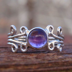 May include: A silver ring with a purple amethyst gemstone set in a delicate, swirling design.