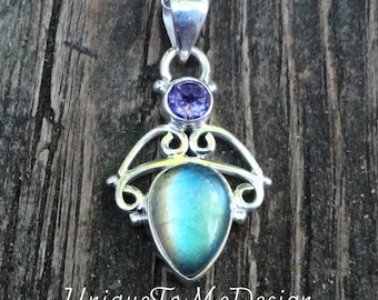 May include: A silver pendant necklace with a teardrop-shaped labradorite gemstone and a small purple amethyst gemstone. The pendant is set in a delicate silver filigree design.