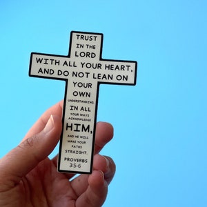 May include: A white cross-shaped sticker with black text that reads "Trust in the Lord with all your heart, and do not lean on your own understanding. In all your ways acknowledge Him, and He will make your paths straight. Proverbs 3:5-6"