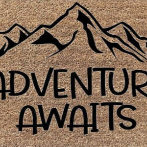 May include: A brown doormat with a black mountain range silhouette and the text "Adventure Awaits".