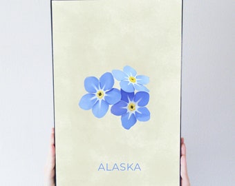 May include: A framed print with a light yellow background featuring a cluster of blue forget-me-not flowers with yellow centers. The word "ALASKA" is printed in black at the bottom of the print.
