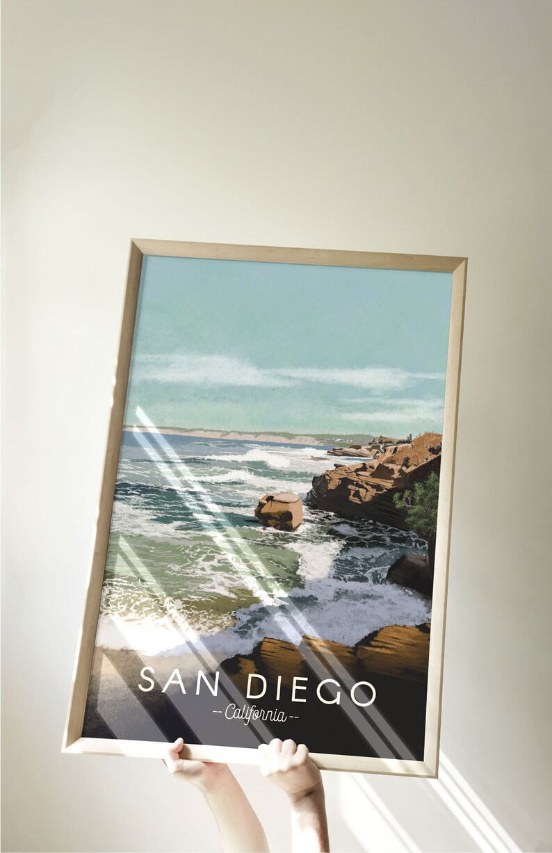 以下が含まれることがあります： サンディエゴ、カリフォルニアのビーチシーンを描いたヴィンテージな旅行イラストの額装ポスター。ポスターには青い空、白い雲、そして波が打ち寄せる岩だらけの海岸線が描かれている。ポスターの下部には黒い背景に白い文字で「SAN DIEGO - California -」と印刷されている。