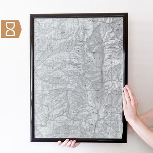 May include: A black framed print of a vintage map of the Sequoia National Park in California. The map shows the park's topography with contour lines and labels for various features, including mountains, rivers, and trails.