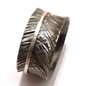 Può includere: Un anello largo in argento con una finitura testurizzata martellata. L'anello ha una sottile fascia d'argento inserita nella fascia più larga.