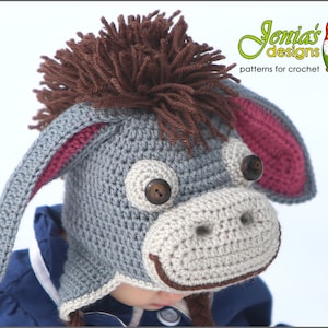 May include: A grey crocheted donkey hat with brown yarn for the mane and pink ears. The hat has brown button eyes and a brown crocheted nose.