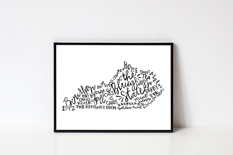 May include: A black framed print featuring a white graphic of the state of Kentucky. The state outline is filled with black text including "Bourbon", "Bluegrass State", and "Kentucky Derby". The print is displayed against a white background.
