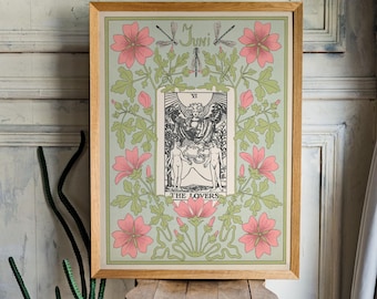 Op de afbeelding: Een ingelijste kunstdruk met de tarotkaart De Geliefden. Het kunstwerk heeft een lichtgroene achtergrond met roze bloemen en groene bladeren. De lijst is van lichtgekleurd hout. De print wordt getoond op een kleine houten kruk.