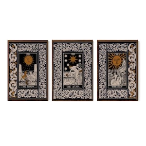 May include: Three framed tarot card prints. Each features a dark background with ornate white and gold borders. The cards depict the Moon, Star, and Sun, with illustrations of a wolf, a nude figure, and a sun-faced figure with a winged horse.