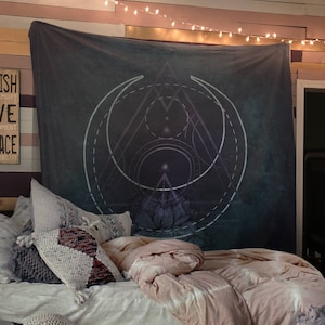 Puede incluir: Un tapiz azul oscuro con un dise&ntilde;o geom&eacute;trico que presenta un c&iacute;rculo, un tri&aacute;ngulo y una flor de loto. El tapiz est&aacute; colgado en una pared con luces de cadena encima. El tapiz est&aacute; en un dormitorio con una cama y almohadas.