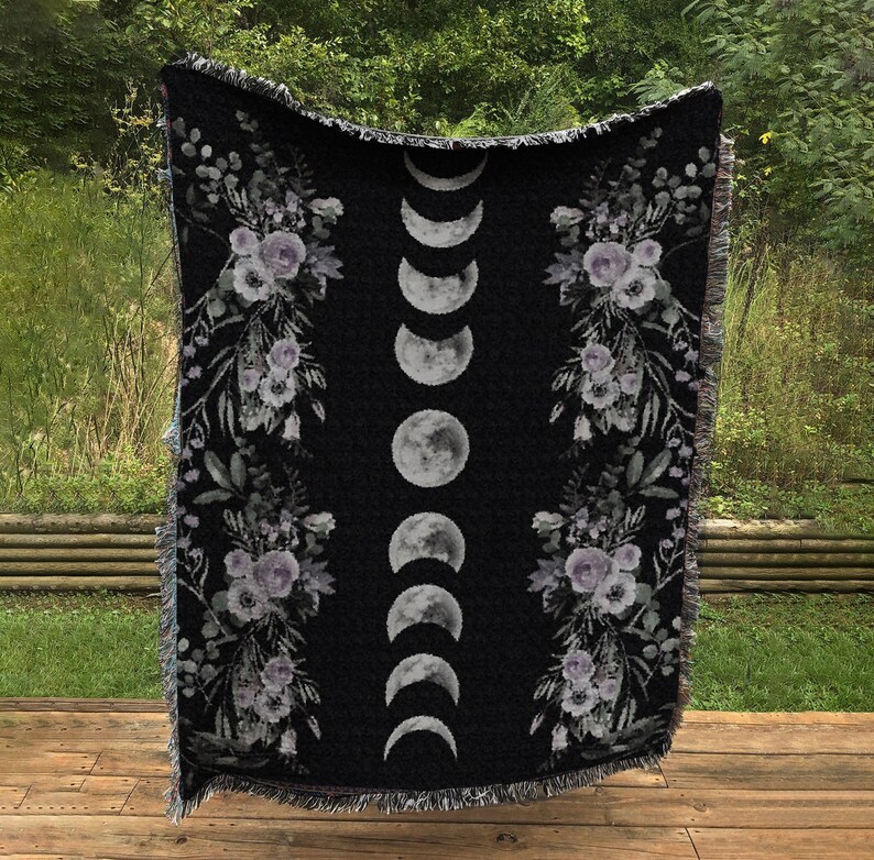 May include: Black woven throw blanket with a floral pattern and a moon phase design. The blanket has a fringe border.