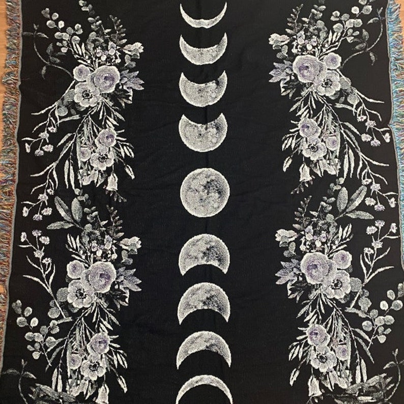 May include: Black woven throw blanket with a white floral pattern and a vertical row of white crescent moons.