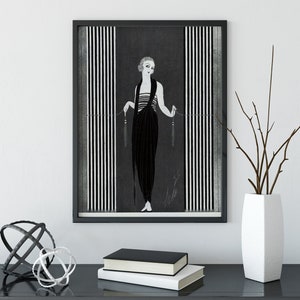 May include: Framed monochrome art print featuring a woman in a long dress, set against vertical striped panels. The artwork is in a black frame. A white vase with branches, a decorative sphere, and books are on a black table.