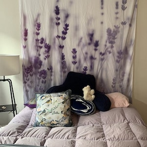 May include: A bed with a lavender floral tapestry headboard, a white and blue throw pillow with the text "La Vie est Belle", a pink throw pillow, a navy blue throw pillow with a white Penn State logo, and a white stuffed bear.