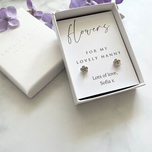 May include: A white gift box with a silver flower earring set inside. The box has a handwritten message that reads "Flowers for my lovely nanny. Lots of love, Sofia x".