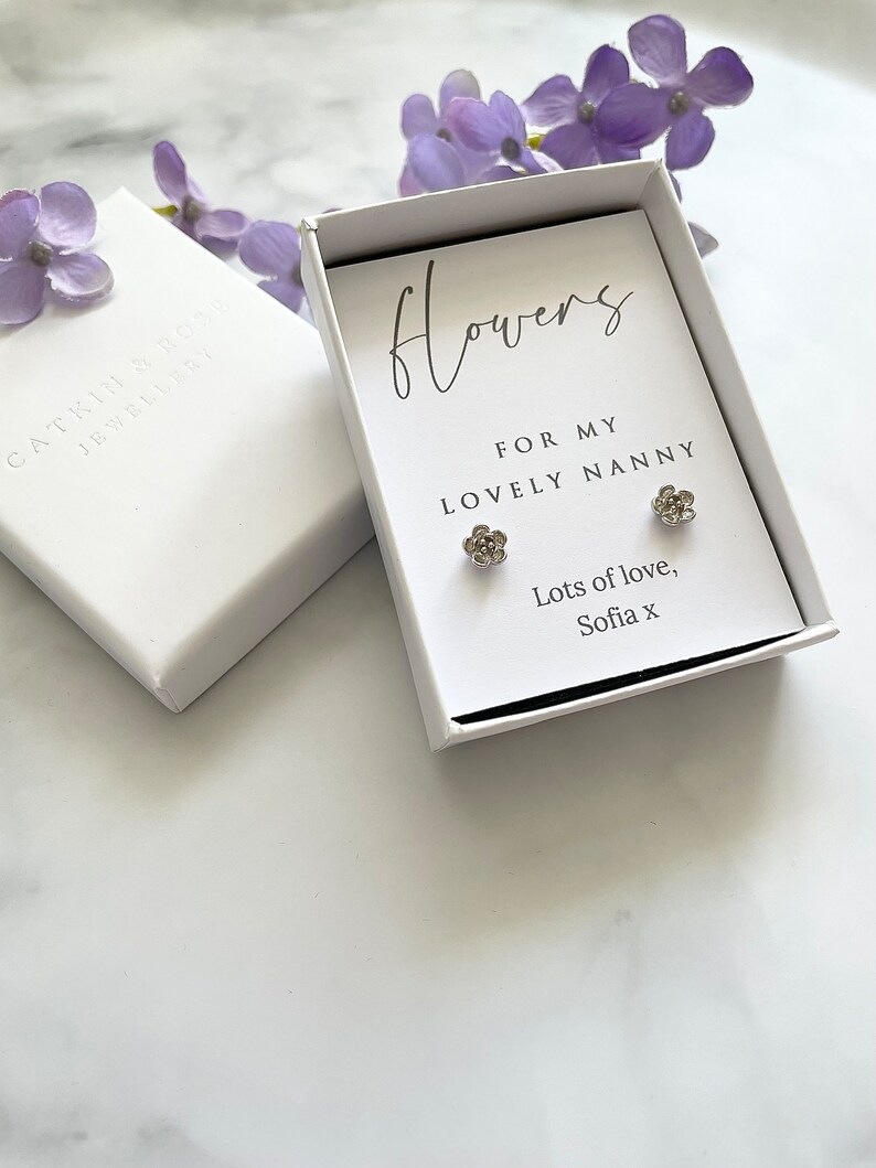 May include: A white gift box with a silver flower earring set inside. The box has a handwritten message that reads "Flowers for my lovely nanny. Lots of love, Sofia x".