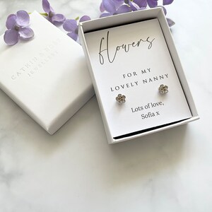 May include: A white gift box with a silver flower earring set inside. The box has a handwritten message that reads "Flowers for my lovely nanny. Lots of love, Sofia x".
