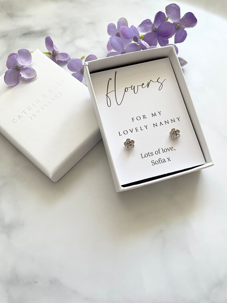 May include: A white gift box with a silver flower earring set inside. The box has a handwritten message that reads "Flowers for my lovely nanny. Lots of love, Sofia x".
