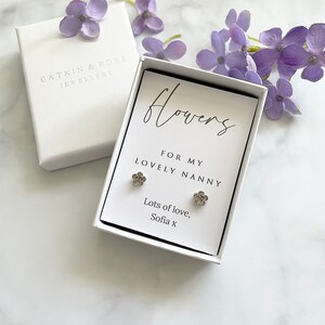 May include: A white gift box with a silver flower earring set inside. The box has a white card with the text "flowers for my lovely nanny lots of love, Sofia x".