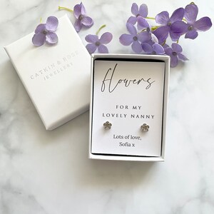 May include: A white gift box with a silver flower earring set inside. The box has a white card with the text "Flowers for my lovely nanny. Lots of love, Sofia x".