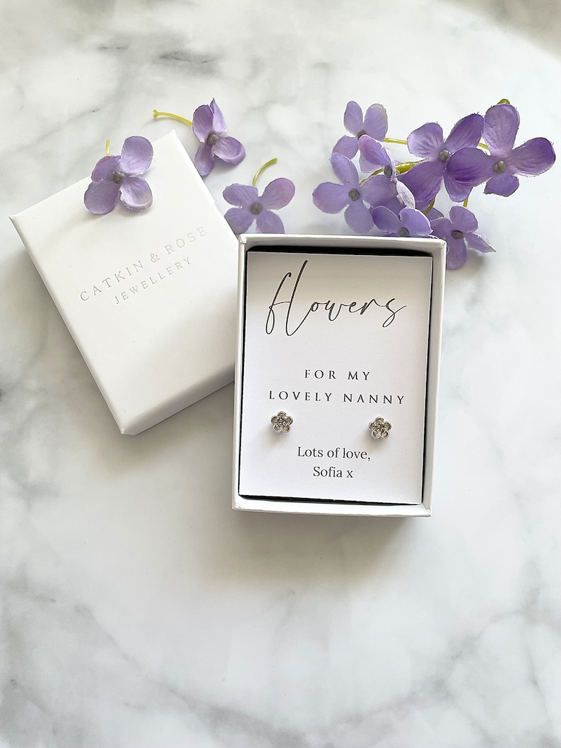 May include: A white gift box with a silver flower earring set inside. The box has a white card with the text "Flowers for my lovely nanny. Lots of love, Sofia x".