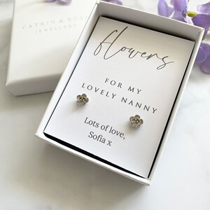 May include: A white gift box with a card that reads "flowers for my lovely nanny" and "lots of love, Sofia x". The box contains a pair of silver flower stud earrings.