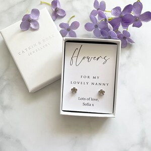 May include: A white gift box with a silver flower earring set inside. The box has a white label with the text "Flowers for my lovely nanny" and "Lots of love, Sofia x".